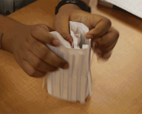 Animated graphic depicts a pair of hands manipulating a piece of corrugated paper. It curls one way, then another, and is able to flex open and closed