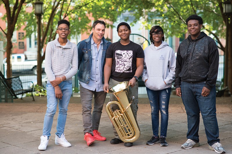 Four students and a teacher stand for a photo, one of the students holds a tuba