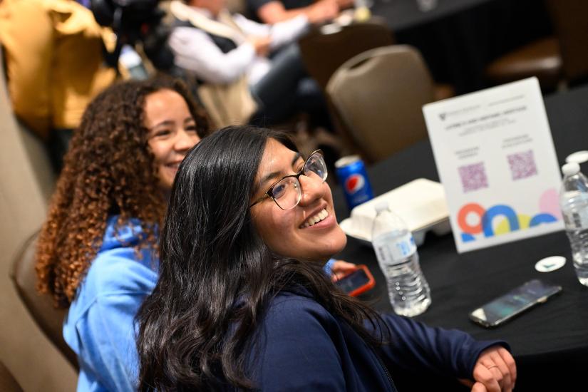 Two young women smile while listening to a presenter