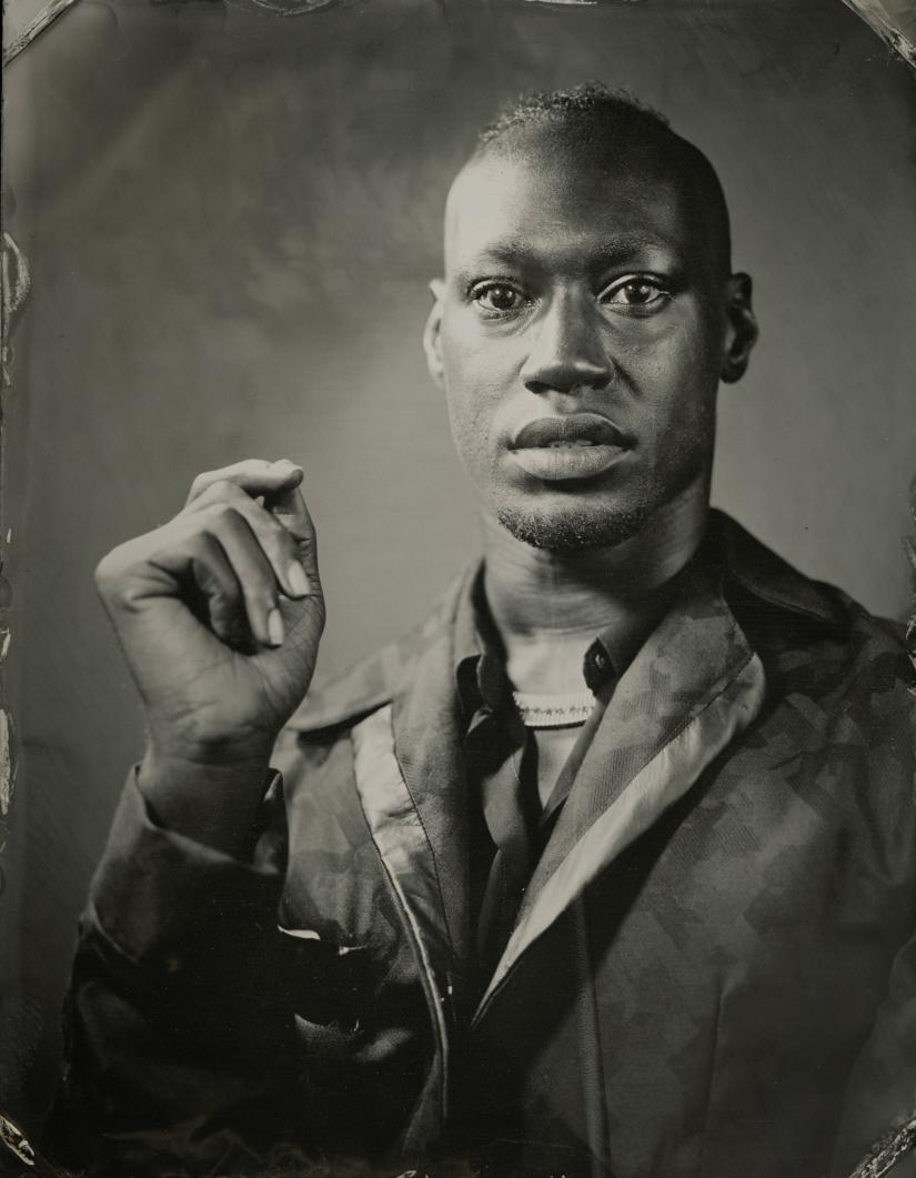 A tintype image of a person wearing a tuxedo jacket and gesturing with their hands