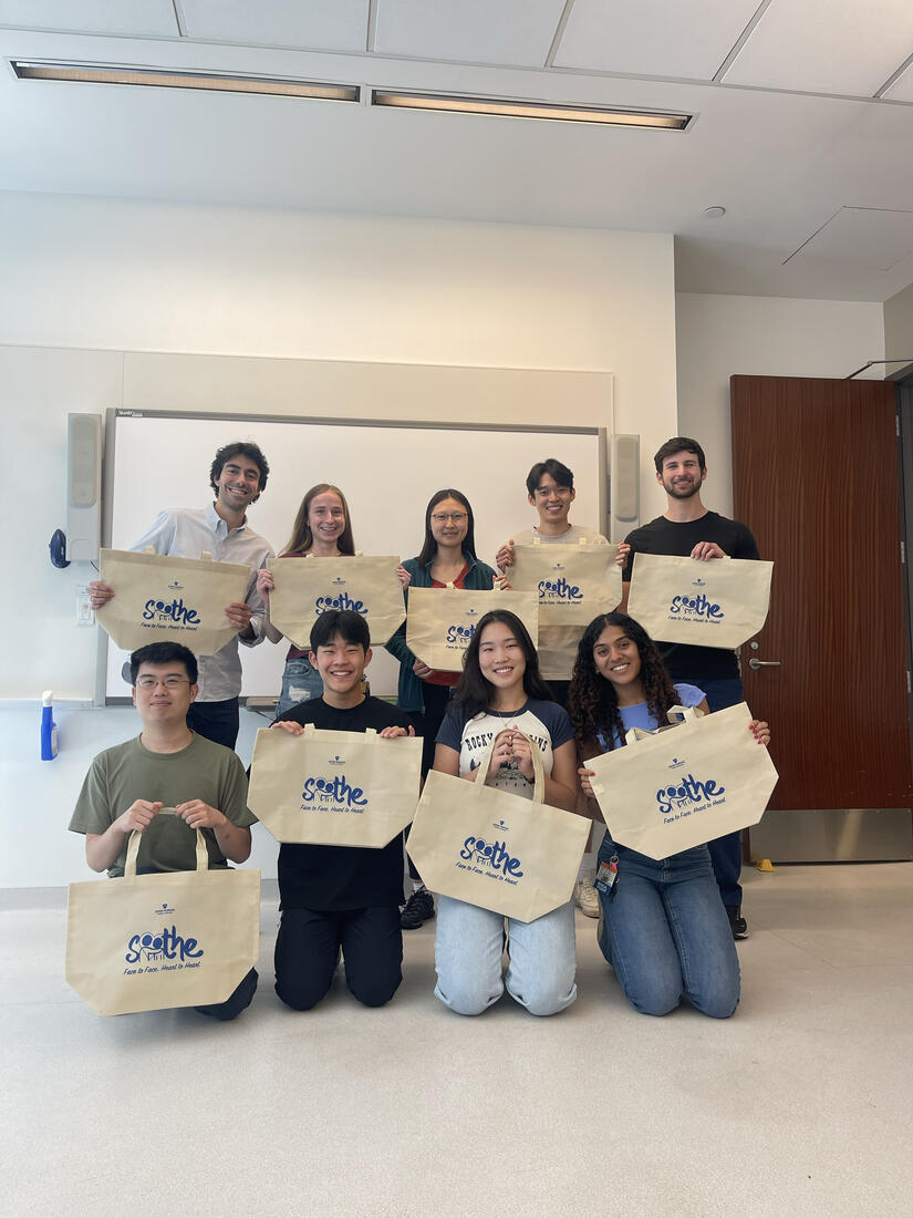 Student volunteer with SOOTHE hold up canvas tote bags in a group photo