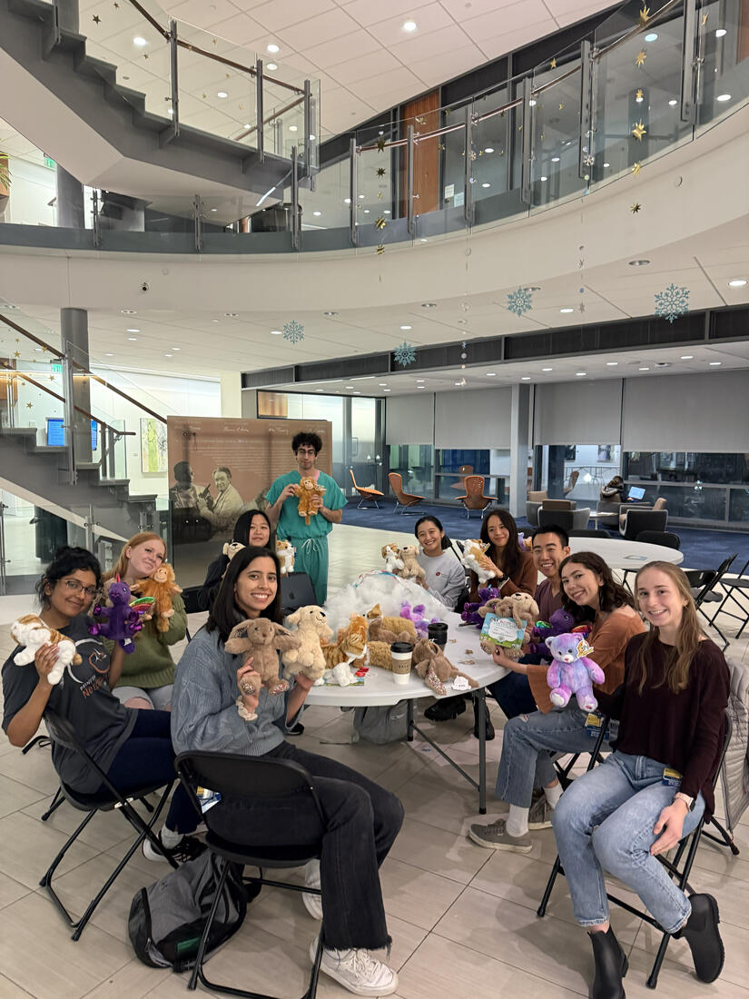 Student volunteer with SOOTHE hold up stuffed animals for patients in a group photo