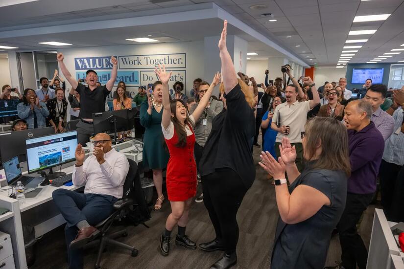 A woman in a red dress holds her hands up as dozens of others around her celebrate