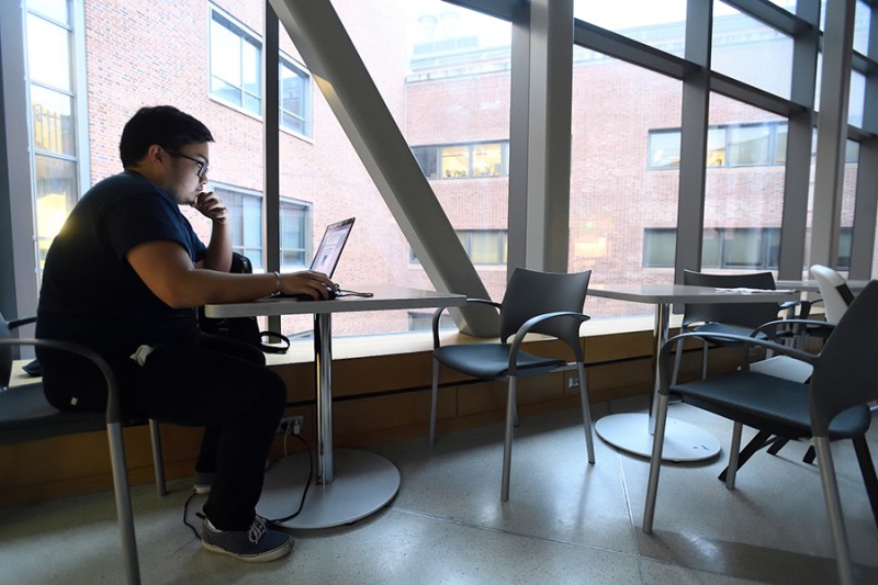 A student sits against a floor-to-ceiling window while morning light streams in