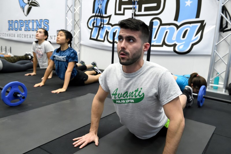 A group of students do a cobra pose in yoga, laying on their stomachs with their hips pressed to the ground and lifting the chests off the ground