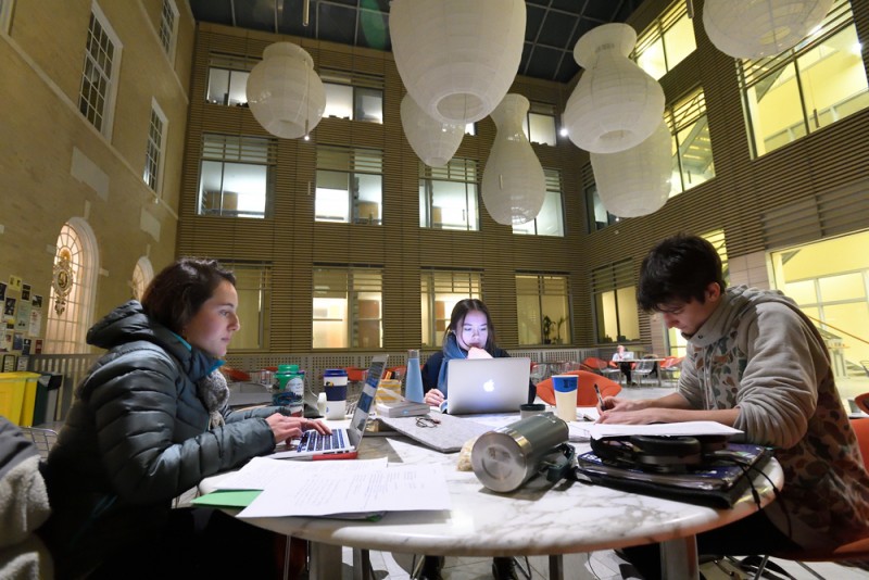 A group of students wear coats and study around a table