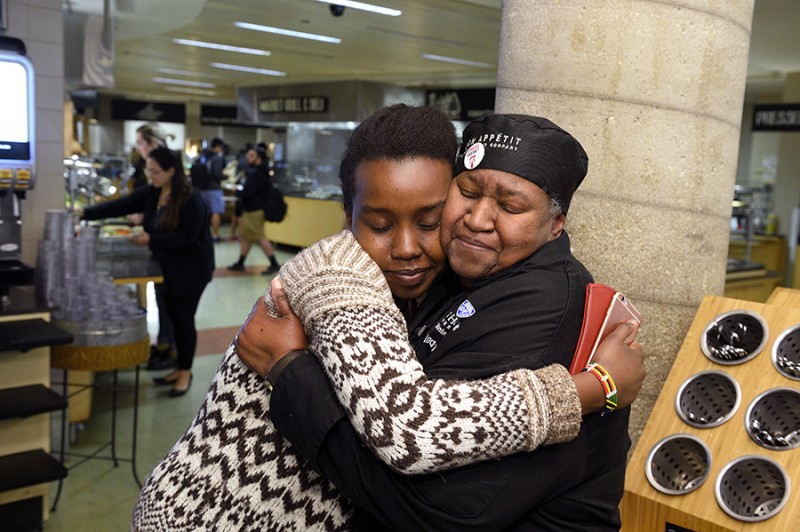 A women wearing an Aramark Dining uniform hugs a student tightly. Both of their eyes are closed.