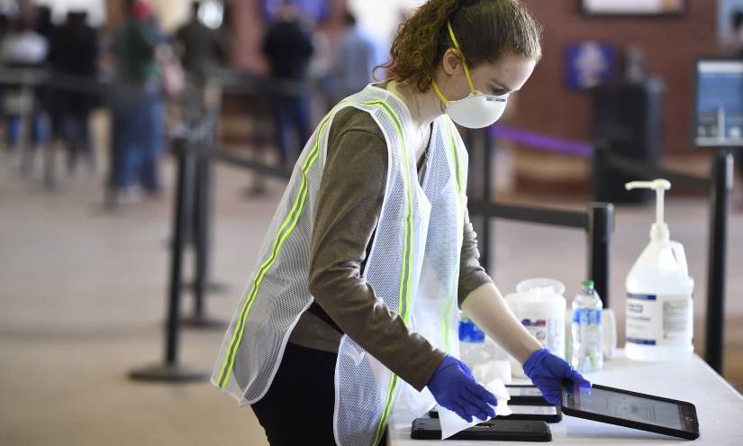 A student volunteer wipes down iPads used during vaccine patient intake