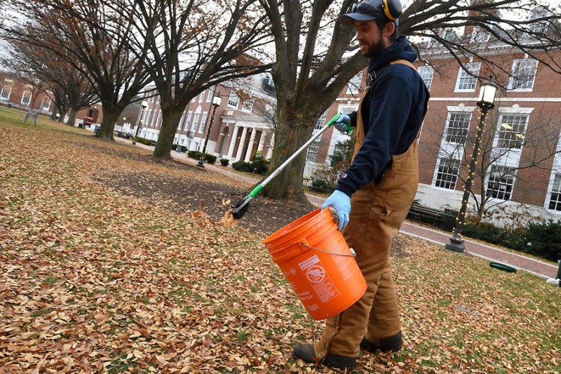 A man in brown carhartt overalls picks up debris with a scooper