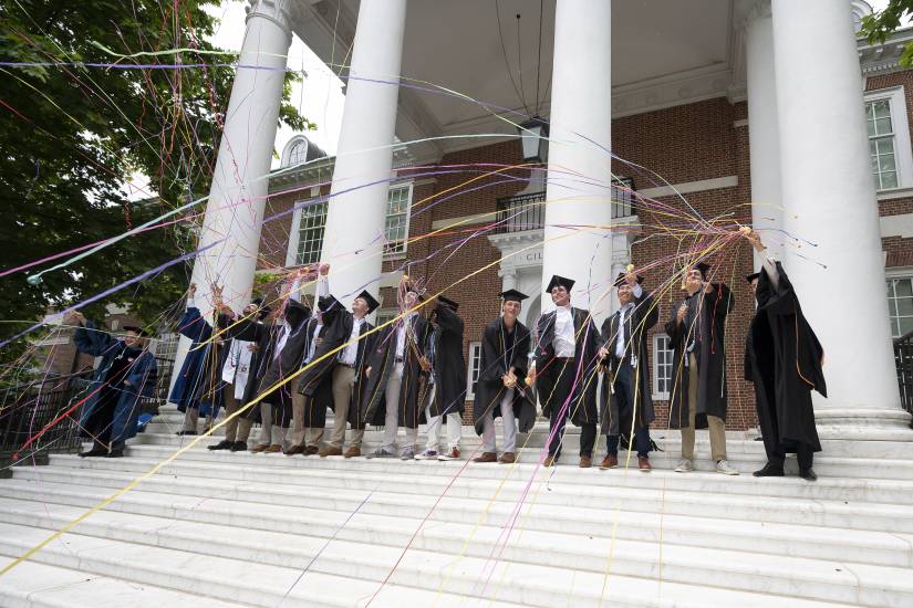 A group of men in Commencement regalia throw streamers