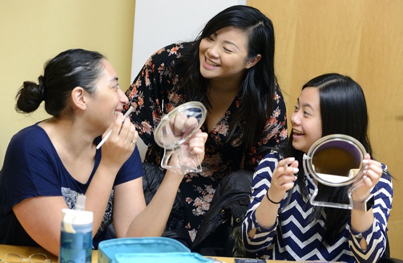 Two students and teacher smiling with makeup brushes and mirrors in hand