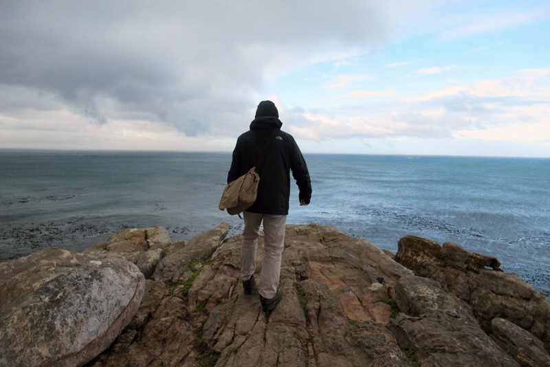 A man stands with his back to the camera facing out over the sea