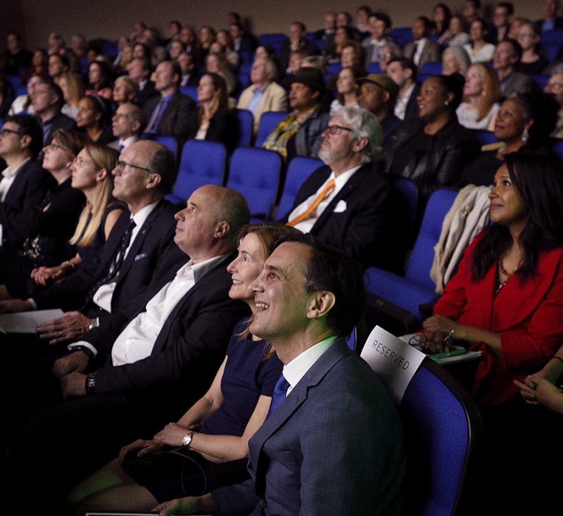 The faces of President Daniels and his wife, Joanna Rosen, are illuminated as they look at a movie screen