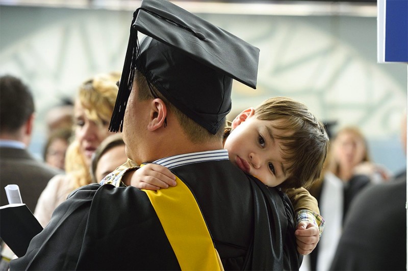 Young boy rests on his father's should during graduation ceremony