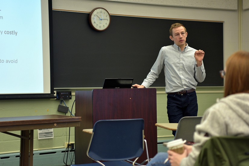 John Hickey leans on a podium while he teaches