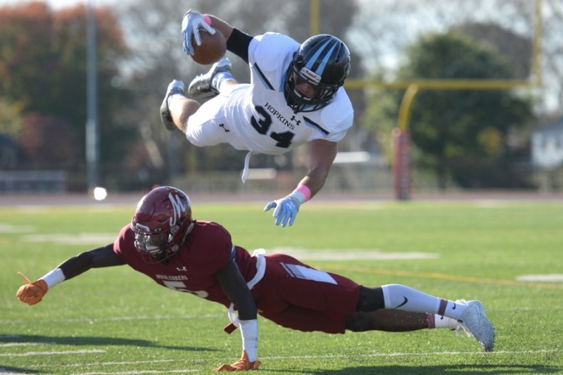 Hopkins player holding football seems to fly over top of a Muhlenberg player who is landing on the ground.