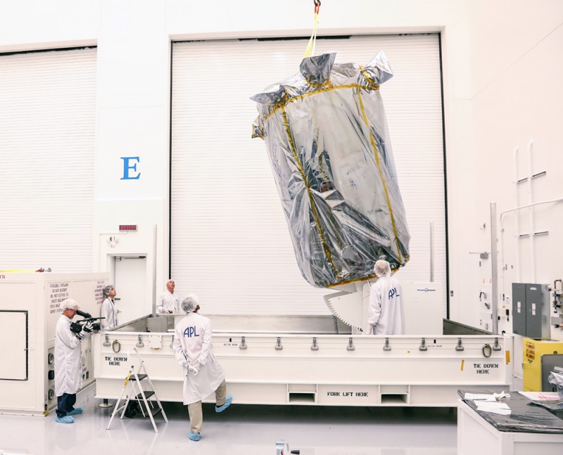 Scientists observe as a giant piece of equipment shrouded in aluminum foil is lifted by crane into a container