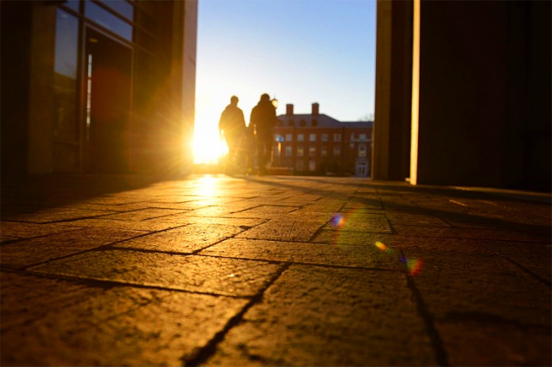 The sun peeks up as two students walk through the breezeway