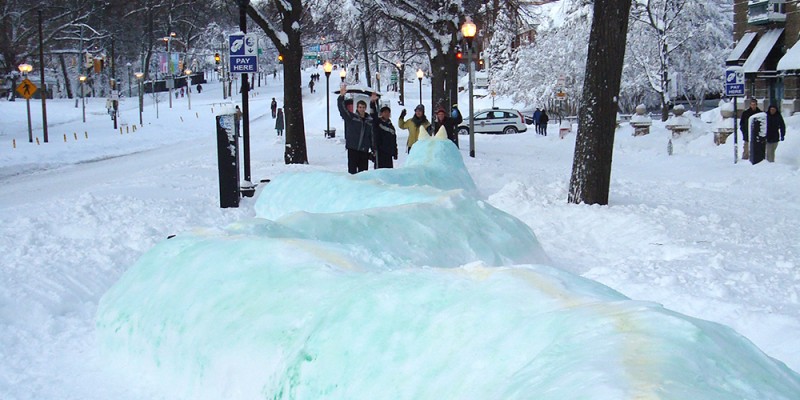 A gigantic snow dragon stretches along the sidewalk in snow-covered Charles Village