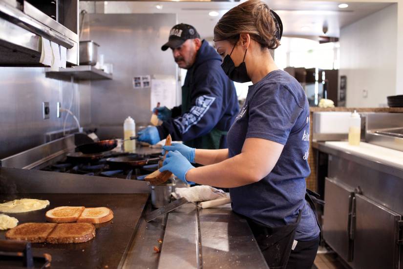 A woman toasts bread on a griddle in an industrial kitchen