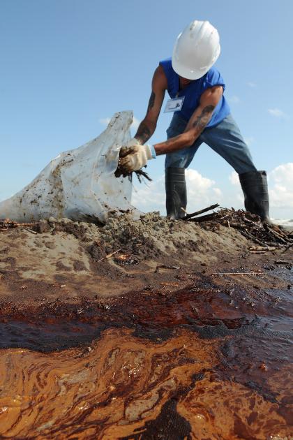 A person scoops oil and mud from the ground into a plastic bag during cleanup for the Deepwater Horizon oil spill