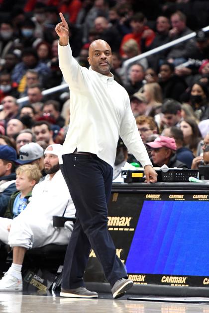 Wes Unseld Jr. walks along the sidelines of a basketball court. In the background are stands full of fans.