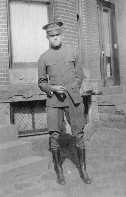 A man in a military uniform stands on a sidewalk in this black and white photo