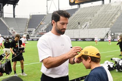 Paul Rabil stands on a lacrosse field while signing a kid's hat