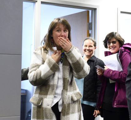 A woman puts her hand to her mouth in surprise while two others in the background smile