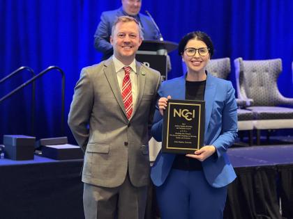 Two people pose for a photo, one holding an NCCI award plaque