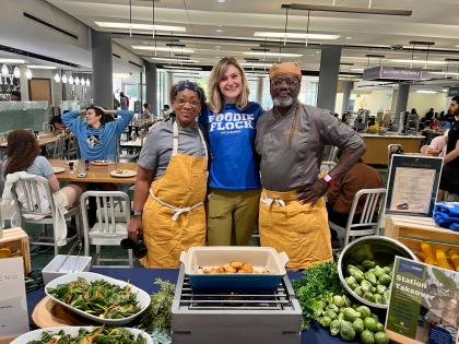 Graham Browning smiles for the camera with Tia and Matthew Raiford in a dining hall at JHU. In front of them is a table of food.
