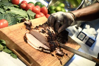 A gloved hand cuts meat on a wooden board