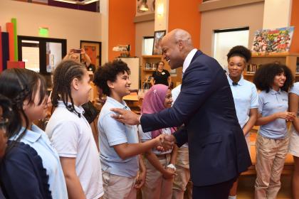 Maryland Governor Wes Moore shakes the hand of a young student in a school uniform.