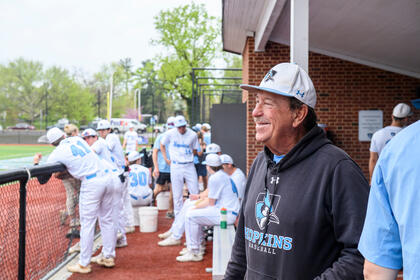 Coach Bob Babb stands in the dugout next to baseball players