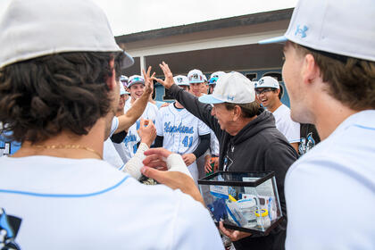 Coach Bob Babb gives a high five while standing in a cluster of baseball players