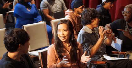 Photograph of a diverse group of people engaging with each other in conversation in an auditorium