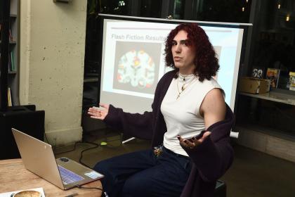 A lecturer talks while sitting in front of a projector screen displaying a brain scan.