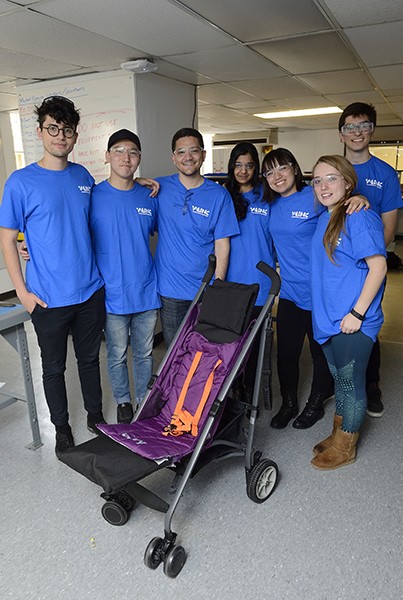 Engineering students in blue shirts pose next to the stroller they designed and built