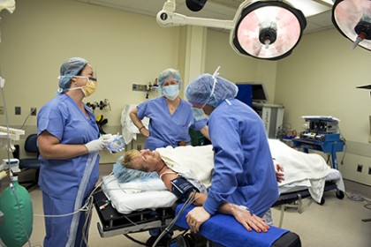 A photo still from <em>The Good Breast</em> shows Doris, in a cap and covered with a cloth, laughing with her surgeon and two nurses in operating clothes