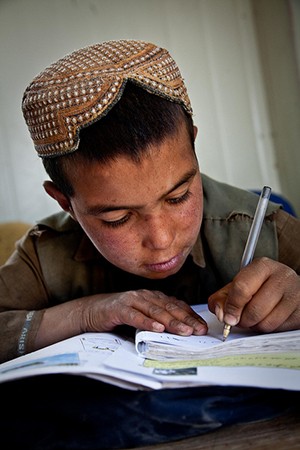 A boy leans over his open textbook and writes with a pen