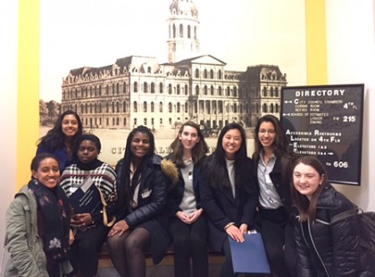 A group of 8 students pose for a photo in front of an image of City Hall