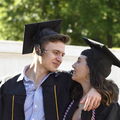 A couple in Commencement regalia pose for a photo
