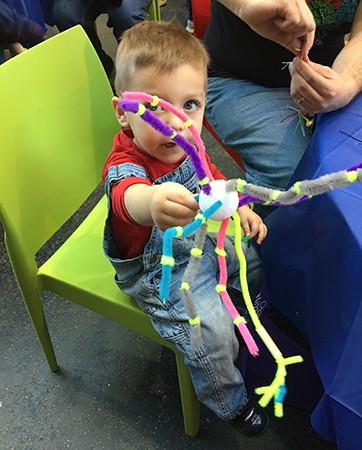 A young boy in overalls hold of a 'neuron' made from a styrofoam ball and pipe cleaners