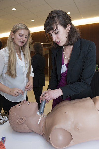 Jordan Kreger watches as Sondra Rahmeh inserts a gray plastic tube into the neck of a medical mannequin 