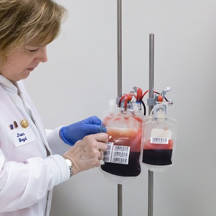 Two plastic-sealed packets of blood hang from a hook while a doctor opens one of the packets