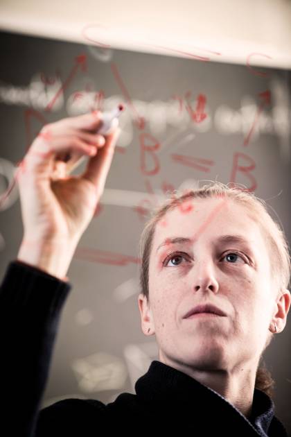 Emily Riehl is photographed through a glass chalkboard as she works on a math problem