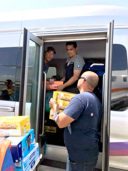 Two men stand inside an airplane and unload boxes of Cheerios and power bars to two people waiting outside the plane
