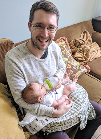 Man smiles while feeding baby from a bottle