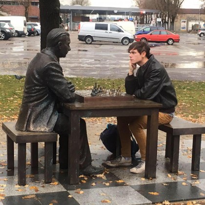 Ian Markham sits at an outdoor table playing chess against a statue