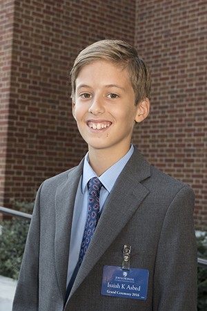 A young boy in a suit and tie smiles at the camera